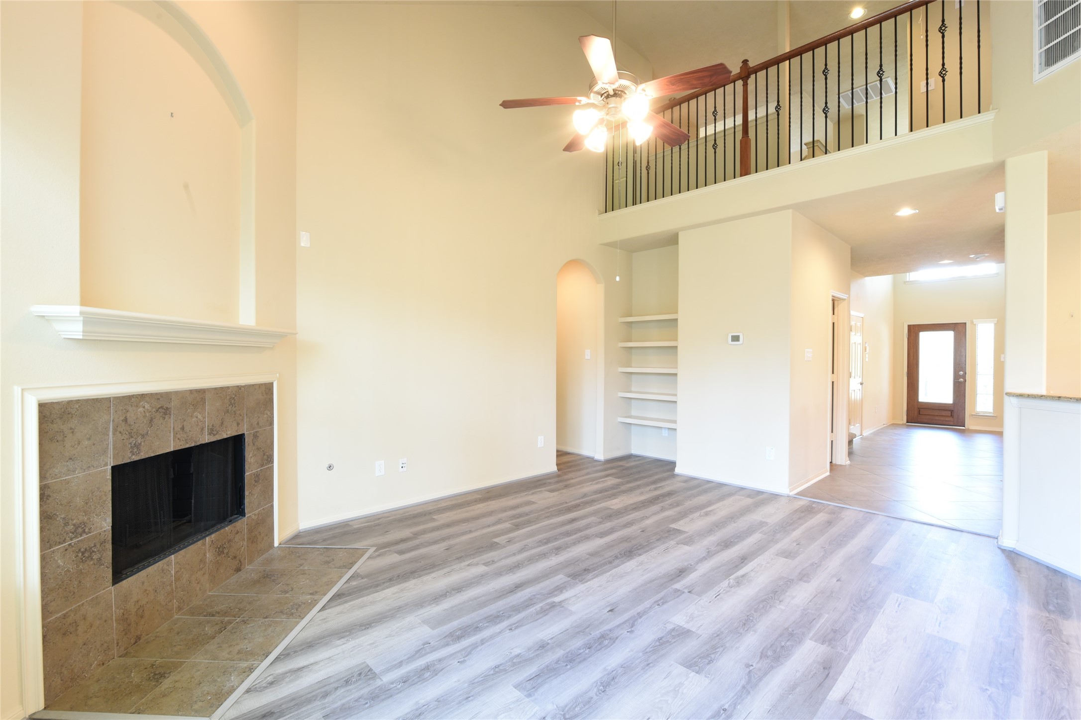 118 East Lasting Spring Circle Spring, TX 77389 - Photo 20 of 46 Spacious living area with high ceilings, elegant fireplace, and a loft-style railing, complemented by sleek flooring and built-in shelving.