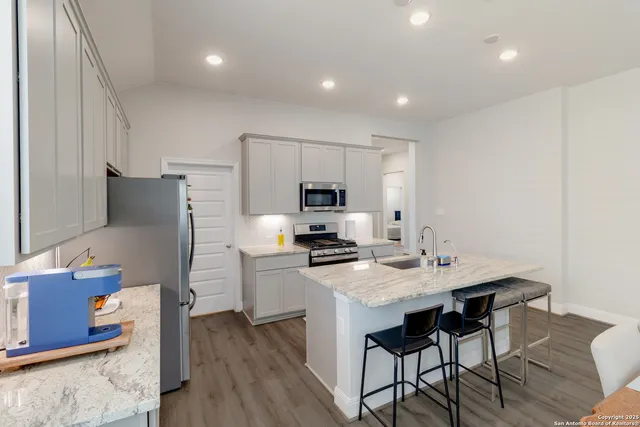 a kitchen with stainless steel appliances granite countertop a stove top oven a refrigerator and a dining table with wooden floor