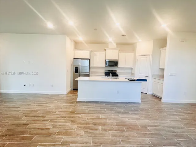 a large kitchen with kitchen island a stove a sink a refrigerator and white cabinets