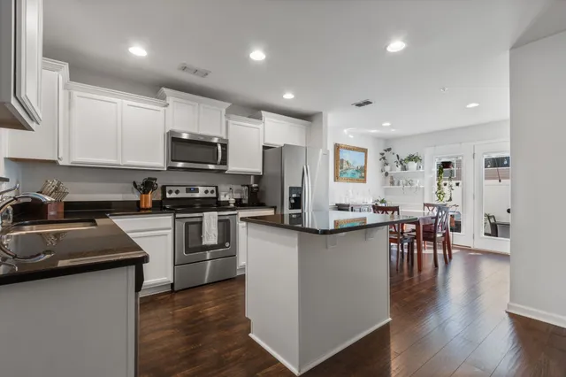 a kitchen with granite countertop a refrigerator stove a sink a dining table and chairs with wooden floor