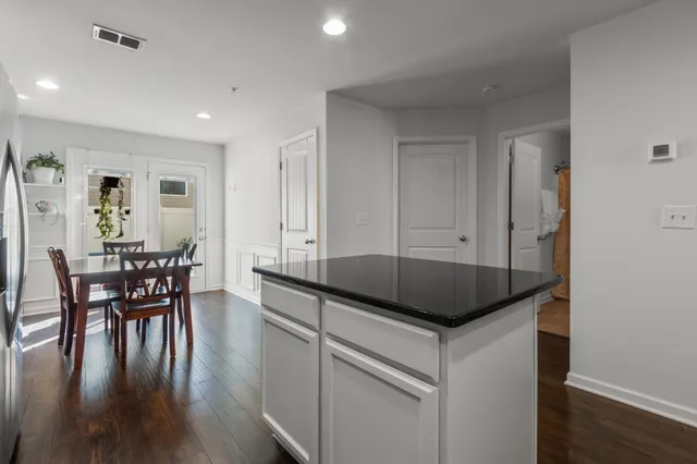 a kitchen with granite countertop kitchen island stainless steel appliances a table chairs sink and wooden floor