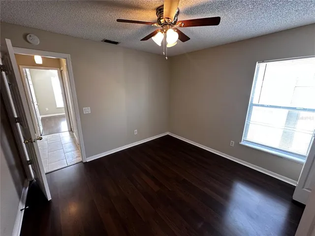 an empty room with wooden floor chandelier fan and windows