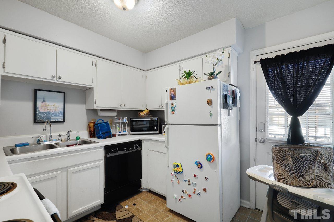 4541 Hargrove Road Raleigh, NC 27604 - Photo 12 of 24 a white kitchen with a refrigerator a stove a sink dishwasher and a dining table with wooden cabinet