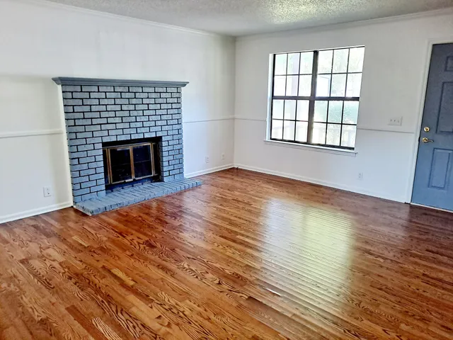 an empty room with wooden floor fireplace and windows