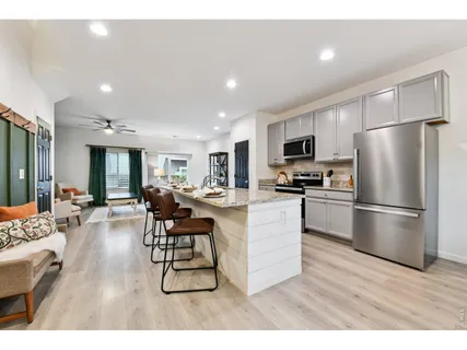 a kitchen with stainless steel appliances kitchen island granite countertop a refrigerator a stove a sink dishwasher a dining table and chairs with wooden floor