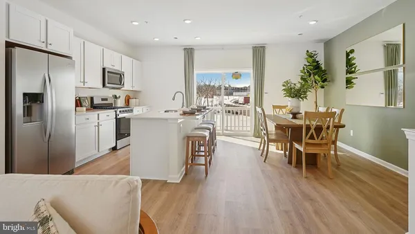 a living room with stainless steel appliances a dining table wooden floor and a view of kitchen
