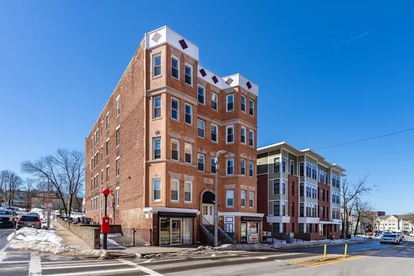 a front view of a building with lot of cars and trees