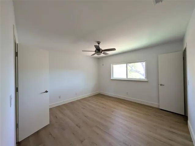 an empty room with wooden floor chandelier fan and windows