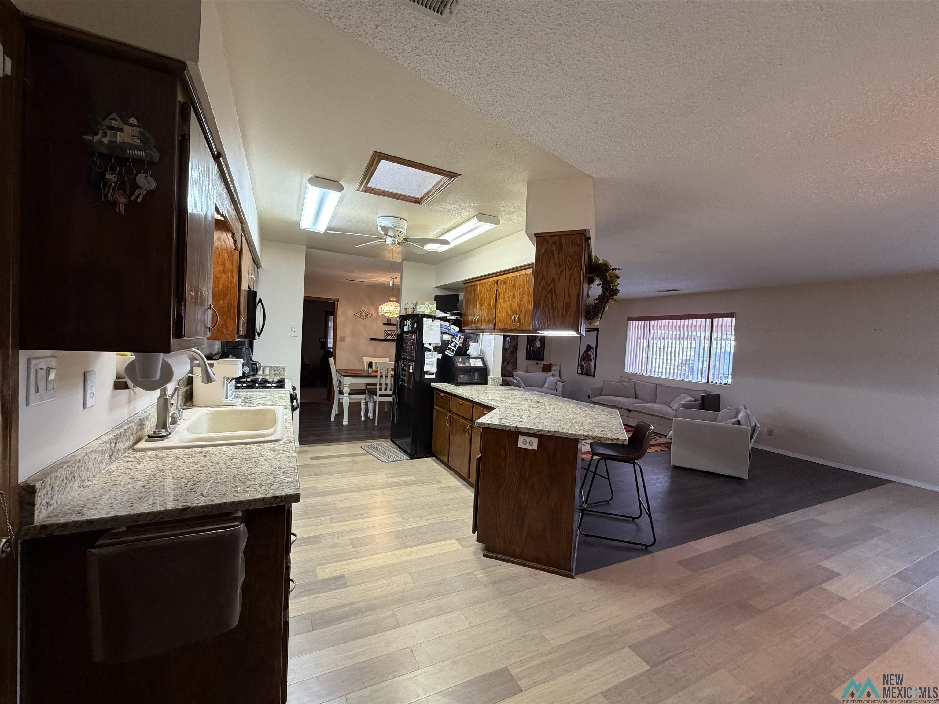 2001 East Derrick Road Carlsbad, NM 88220 - Photo 83 of 84 Kitchen featuring open floor plan, dark wood finish cabinetry, a ceiling fan, light stone countertops, and a kitchen bar