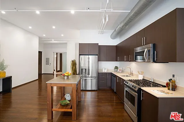 a kitchen with stainless steel appliances granite countertop a refrigerator a stove top oven a sink dishwasher and white cabinets with wooden floor