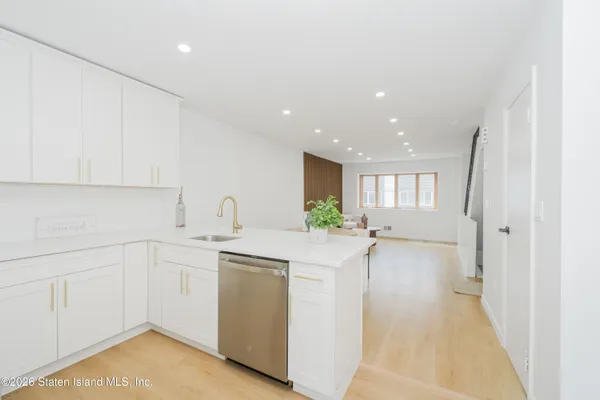 a view of a kitchen with a sink and dishwasher with white cabinets