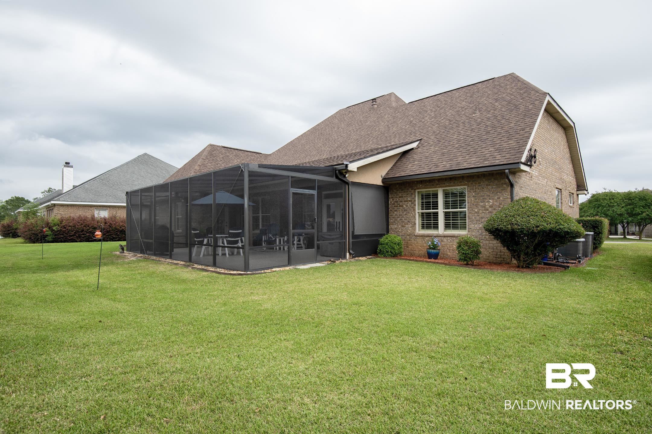9357 Lakeview Drive Foley, AL 36535 - Photo 14 of 68 Brick exterior featuring a screened-in patio with a concrete slab, a brown shingled roof, and a meticulously manicured lawn