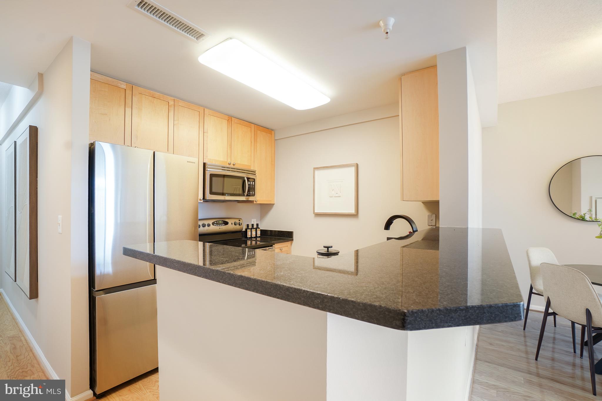 11700 Old Georgetown Road, Unit 214 Rockville, MD 20852 - Photo 14 of 44 a kitchen with stainless steel appliances granite countertop a refrigerator a stove a sink a dining table and chairs with wooden floor