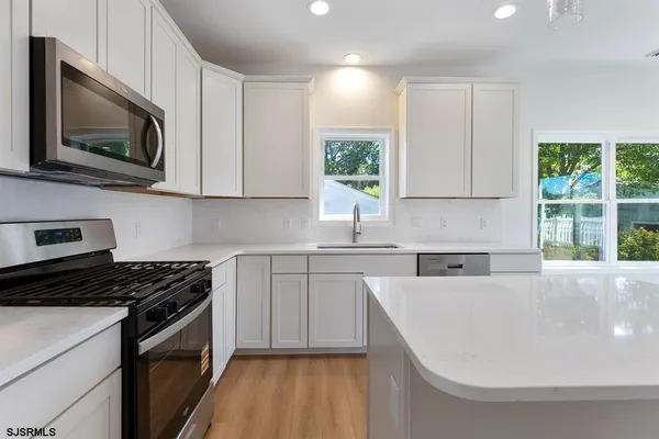 a kitchen with stainless steel appliances granite countertop a sink a stove a microwave a window and white cabinets
