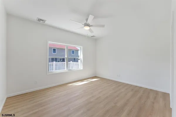 an empty room with wooden floor ceiling fan and windows
