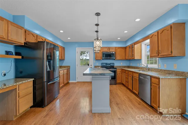 a kitchen with stainless steel appliances kitchen island granite countertop a refrigerator a stove top oven a sink and dishwasher with wooden floor