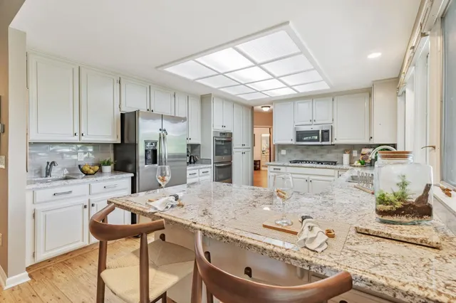 a kitchen with stainless steel appliances kitchen island granite countertop a refrigerator a stove a sink dishwasher and white cabinets with wooden floor