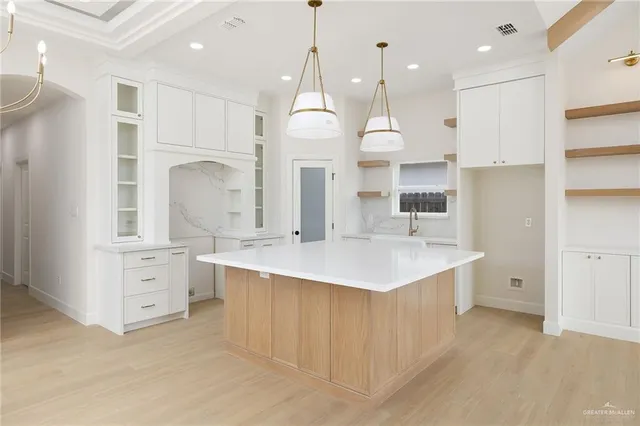 a large white kitchen with a large island oven a stove and a chandelier