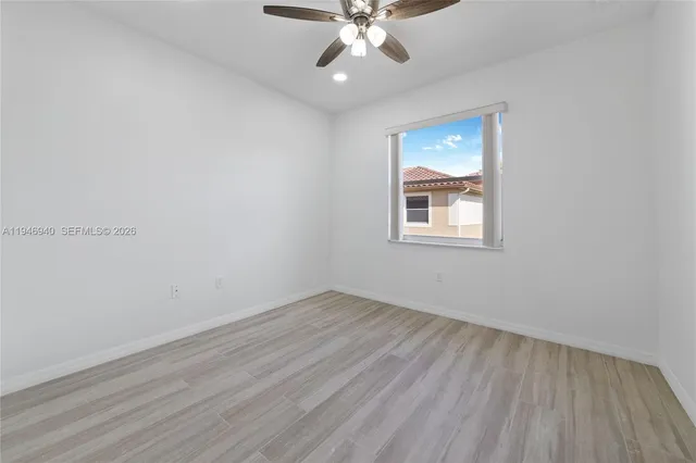 an empty room with wooden floor chandelier fan and windows