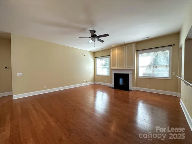 an empty room with wooden floor fireplace and windows