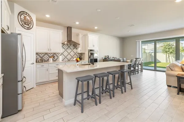 a kitchen with stainless steel appliances kitchen island granite countertop a refrigerator a stove a dining table and chairs with wooden floor