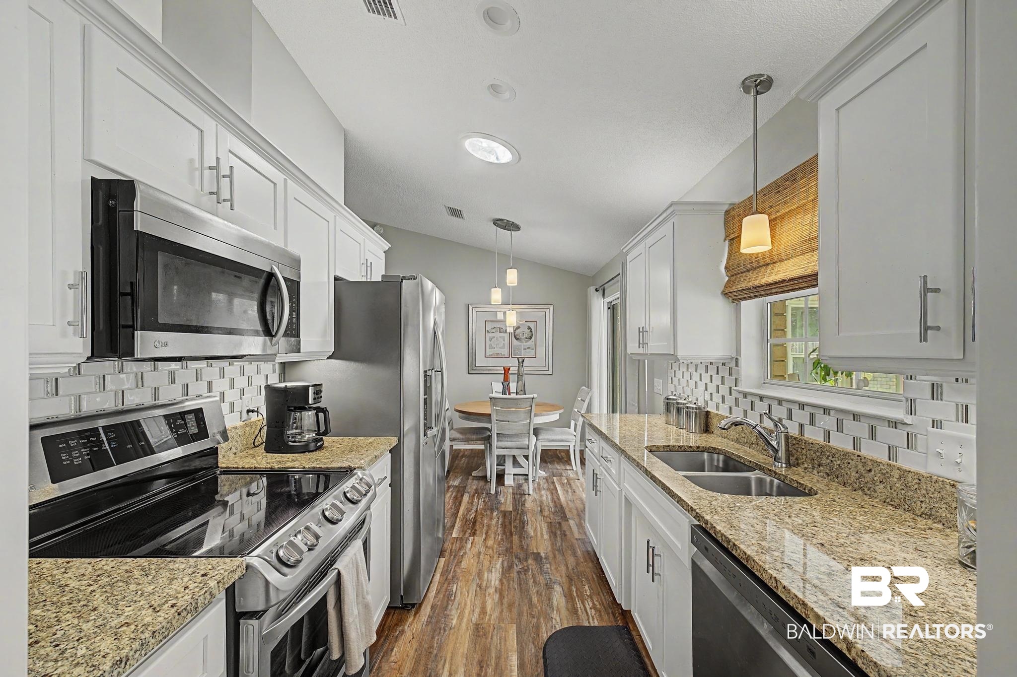 2808 Pine Ridge Drive Lillian, AL 36549 - Photo 14 of 47 Open-concept kitchen featuring white shaker cabinetry, stainless steel appliances, speckled countertops, and wood-finish flooring