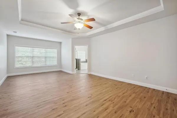 an empty room with wooden floor chandelier fan and windows