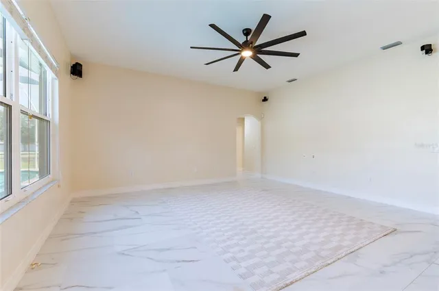 an empty room with chandelier fan and windows