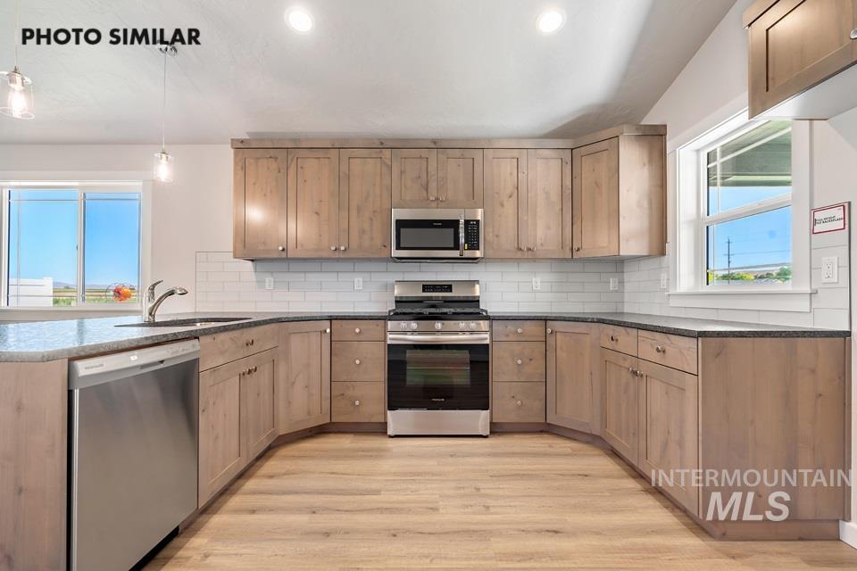 1693 Rapid Road Emmett, ID 83617 - Photo 11 of 28 U-shaped kitchen featuring light wood cabinetry, stone countertops, stainless steel appliances, a subway tile backsplash, and light wood-finish flooring