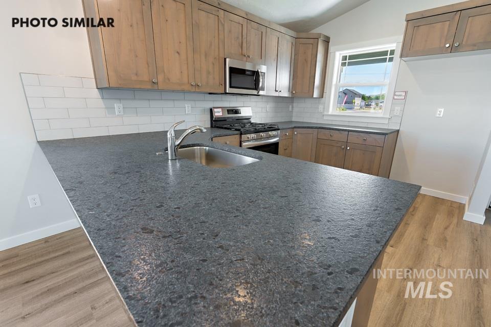 1693 Rapid Road Emmett, ID 83617 - Photo 12 of 28 Spacious kitchen featuring dark, textured countertops, an undermount stainless steel sink with a gooseneck faucet, light wood-finish cabinetry, a white subway tile backsplash, and stainless steel appliances including an oven range and built-in microwave