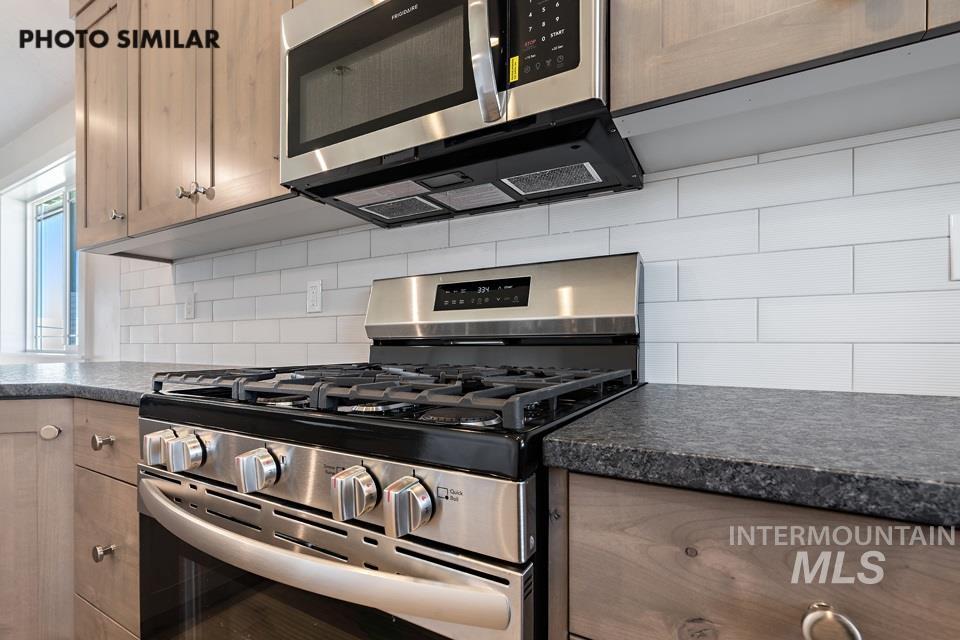 1693 Rapid Road Emmett, ID 83617 - Photo 13 of 28 Modern kitchen featuring stainless steel appliances, a gas range with an overhead microwave, light wood-finish cabinetry, dark speckled countertops, and a white subway tile backsplash