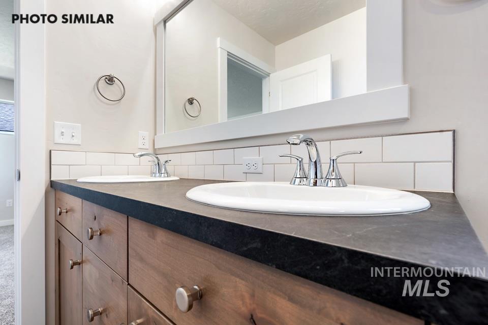 1693 Rapid Road Emmett, ID 83617 - Photo 19 of 28 Dual vanity with wood-finish cabinetry, integrated sinks, dark countertop, and subway tile backsplash