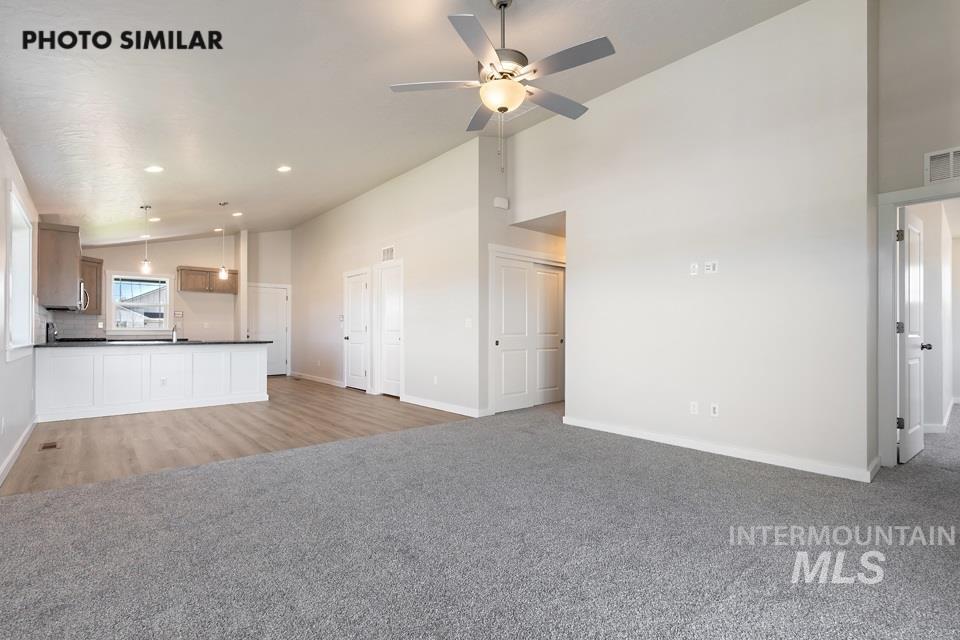 1693 Rapid Road Emmett, ID 83617 - Photo 2 of 28 Open-concept living area featuring vaulted ceilings, a ceiling fan with integrated lighting, and a blend of gray carpet and wood-finish flooring