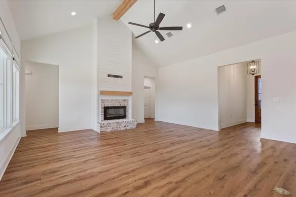 an empty room with wooden floor a ceiling fan a fireplace and windows