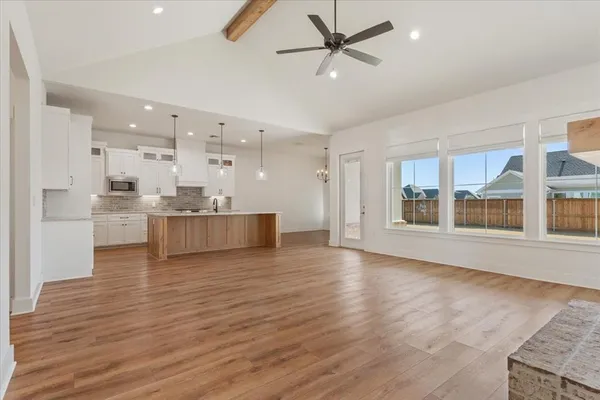 a view of an empty room with wooden floor and a kitchen