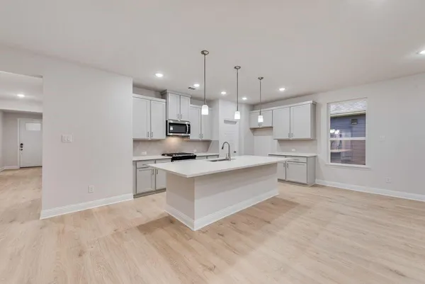a large white kitchen with kitchen island a sink dishwasher a stove a refrigerator and white cabinets with wooden floor