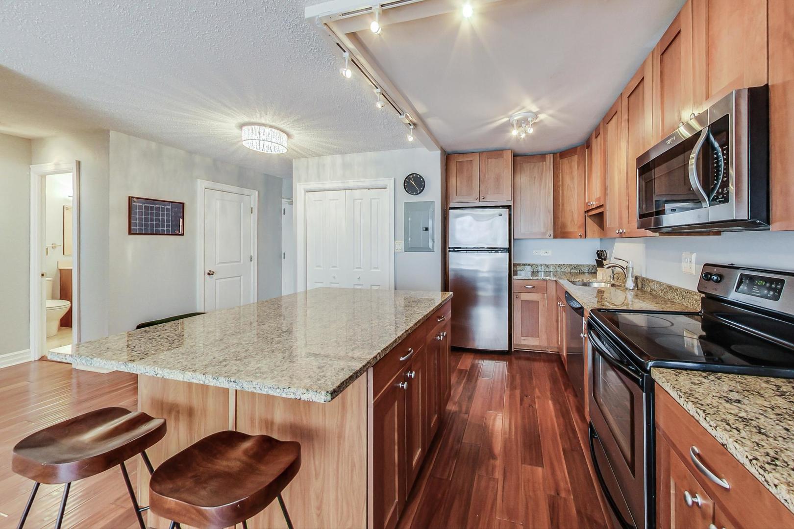 2930 North Sheridan Road, Unit 811 Chicago, IL 60657 - Photo 25 of 52 a kitchen with stainless steel appliances granite countertop a stove top oven a sink dishwasher and wooden cabinets with wooden floor