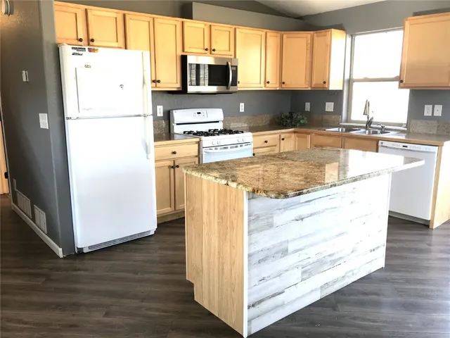 a kitchen with stainless steel appliances granite countertop a refrigerator a stove a sink and a microwave with wooden floor