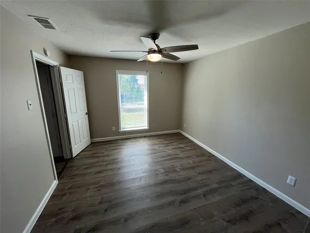 an empty room with wooden floor fan and windows