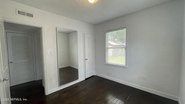 an empty room with wooden floor closet and windows