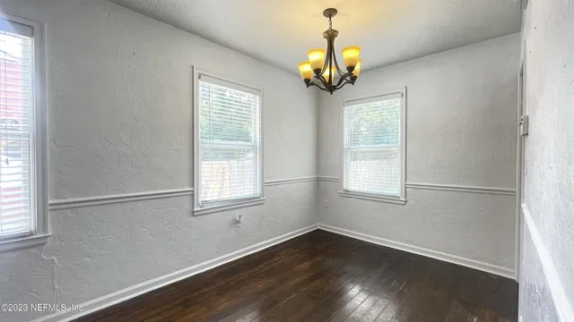 an empty room with wooden floor chandelier and windows