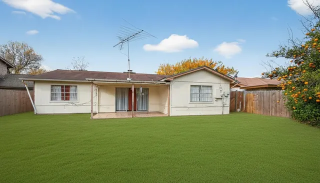 a view of a yard in front of a house with a plants and wooden fence