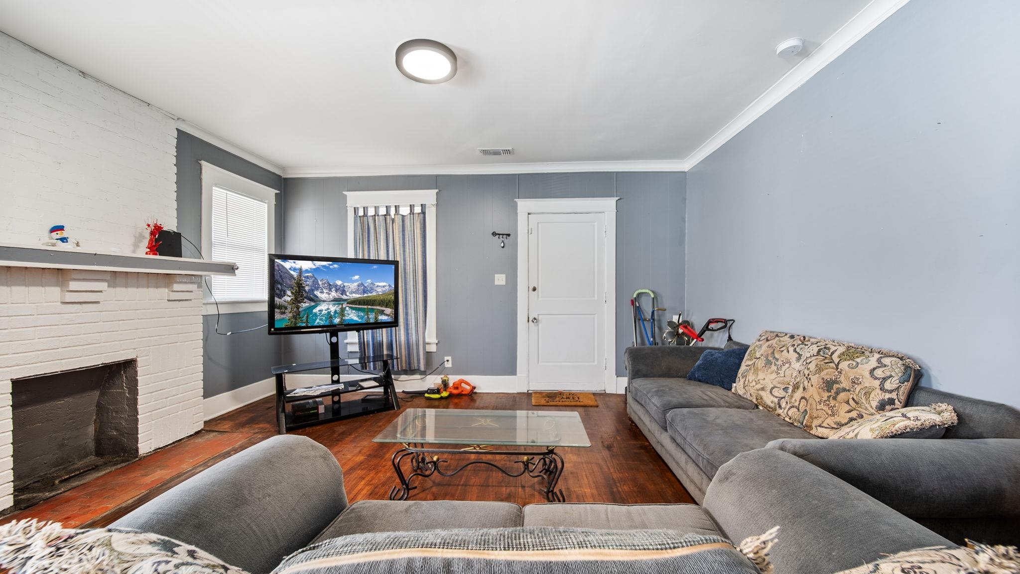 659 Decatur Street Memphis, TN 38107 - Photo 7 of 24 Living area featuring wood-finish flooring, a white brick fireplace, multiple windows with white trim, a flush-mount ceiling light, and crown molding