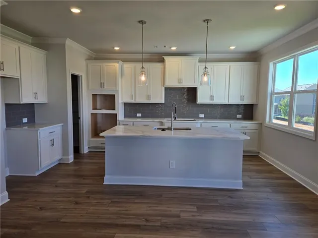 a large kitchen with kitchen island granite countertop a stove a sink a refrigerator and white cabinets with wooden floor