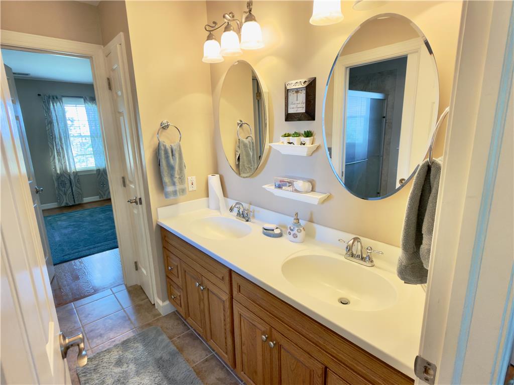 4982 Abbey Road Coplay, PA 18037 - Photo 32 of 55 Oval mirrors hang above a double vanity with wooden cabinetry and tile flooring.