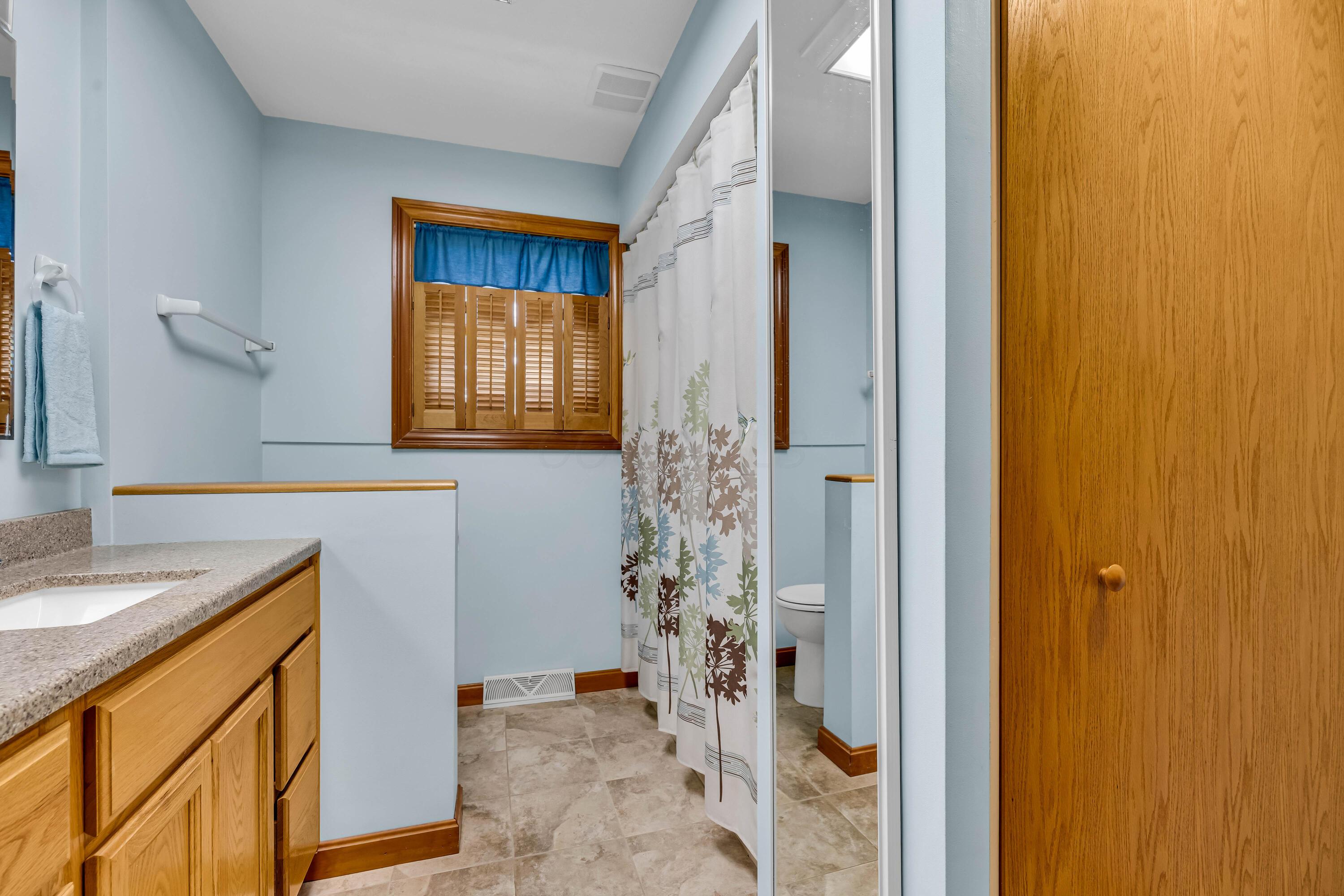 1213 East Cooke Road Columbus, OH 43224 - Photo 26 of 57 • Heated, ceramic tile flooring • Blue painted walls • Linen closet with bi-fold doors • Laundry chute • Enclosed vanity with double bowl, cultured marble sinktop • (2) 2 bulb wall lights • Ceiling light • Tub/shower combination with ceramic tile surround • Window shutters • (2) mirrored medicine cabinets