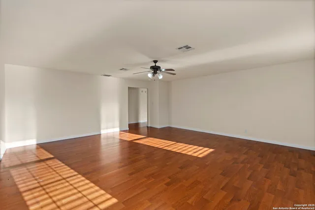 an empty room with wooden floor chandelier fan and windows