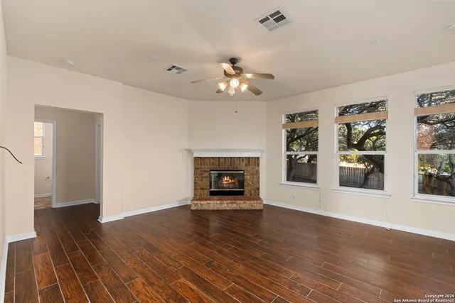 a view of an empty room with wooden floor fireplace and a window