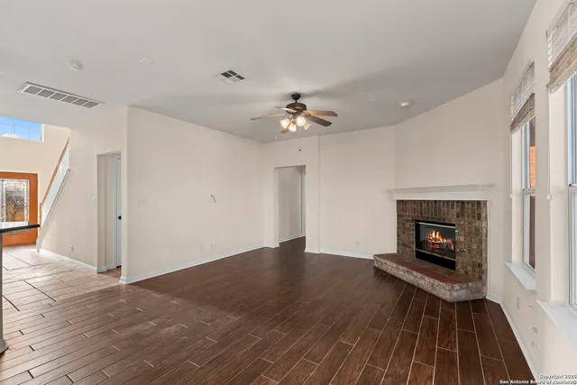 a view of a livingroom with a fireplace a ceiling fan and wooden floor