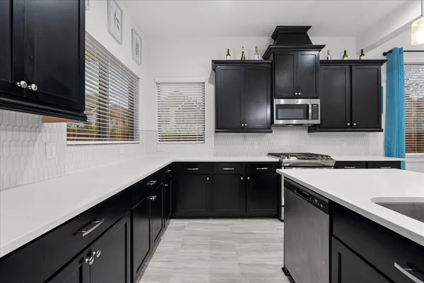 a kitchen with stainless steel appliances kitchen island granite countertop a dining table chairs refrigerator and microwave